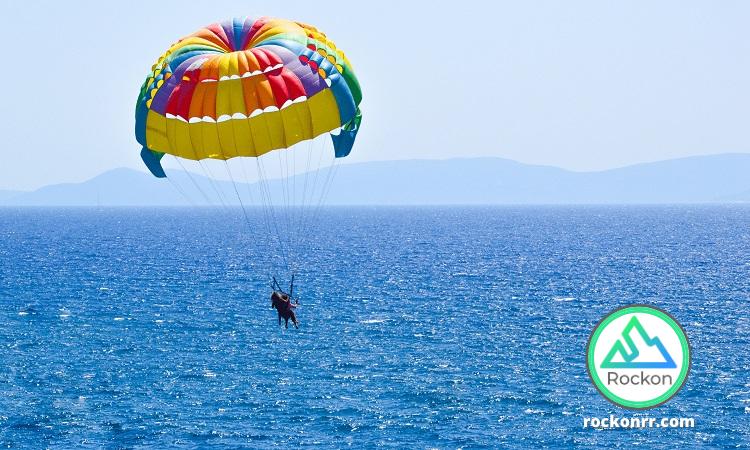 Two passengers suspended in a colorful parachute harness high above a boat on the Atlantic ocean